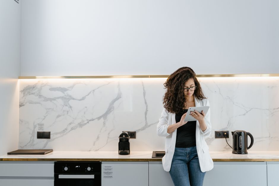 A person sits in a minimalist, modern living room, using a tablet to manage their property listing, illustrating the new wave of tech-driven real estate services.
